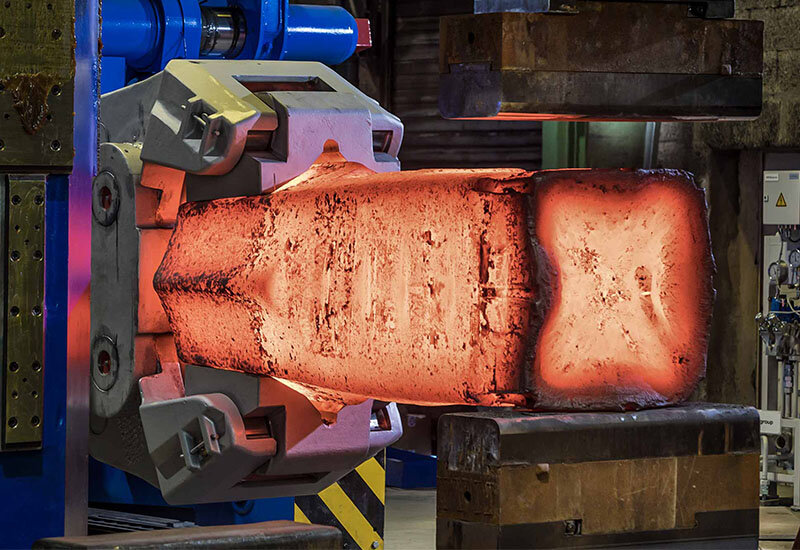 Ansicht von vorne: heißes Metall wird mithilfe eines Schmiedemanipulators gehalten